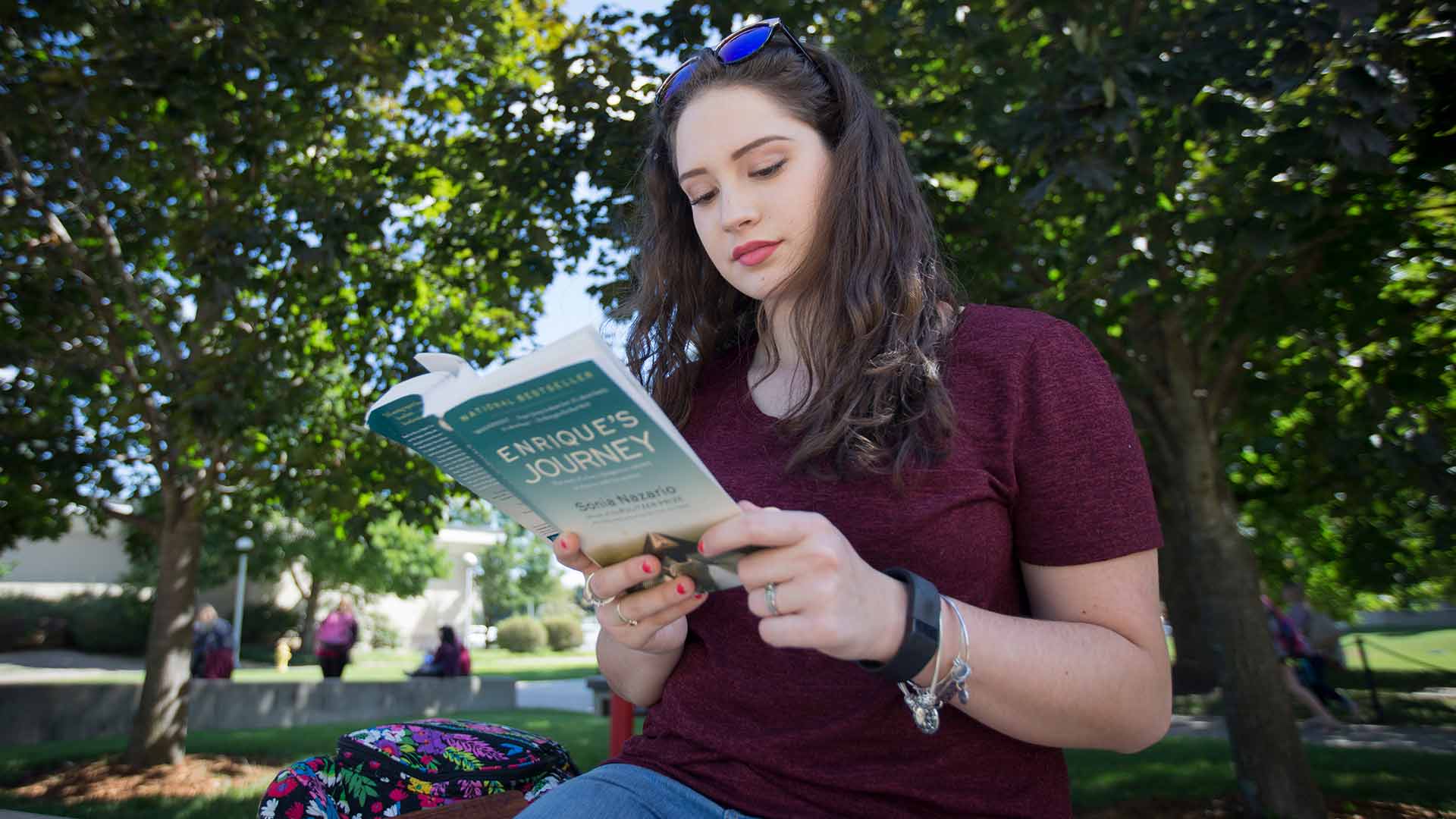 A student reading the book "Enrique's Journey" outside on a nice day on campus.