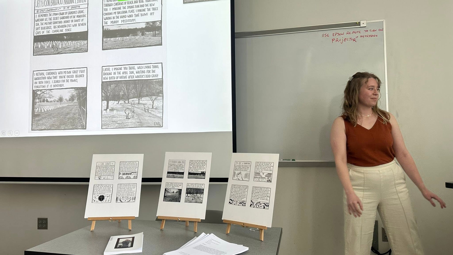 Emily Lewandowski, a English-creative writing master's student, presents her thesis in a classroom, showing written and illustrated panels of her graphic novel.