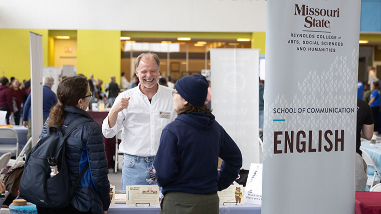 Dr. Alan Tinkler, the English department head, supervises a booth for the department while discussing English programs with two students at a fall showcase.