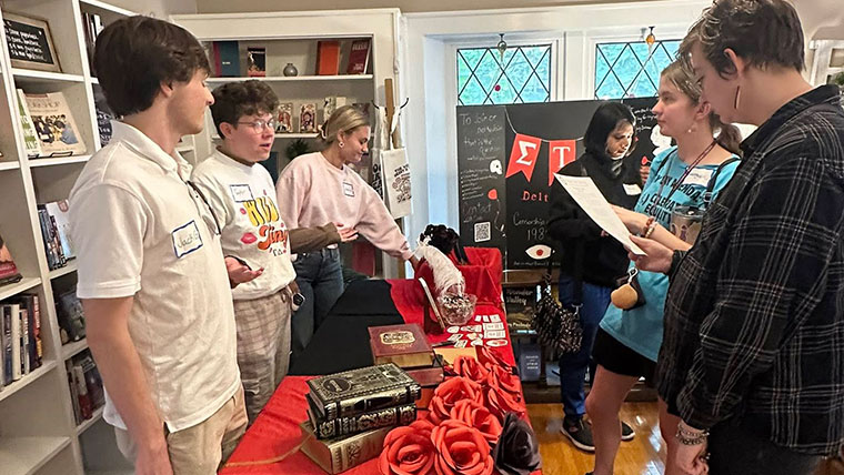 Three members of English-related student organizations set up a table and discuss learning opportunities with prospective students at an open house in a local bookstore.
